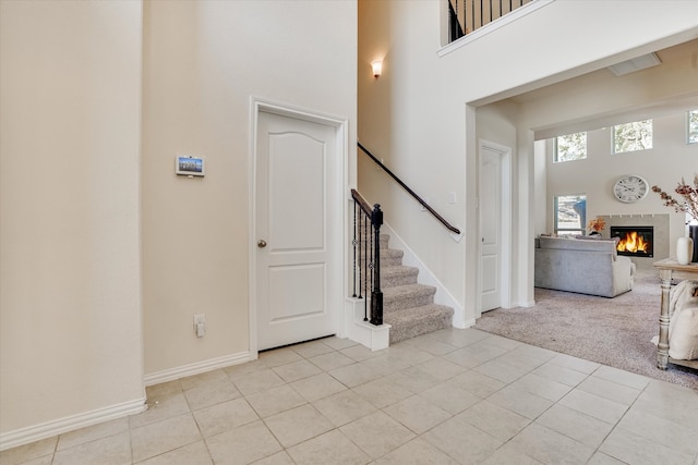 carpeted entrance foyer featuring a towering ceiling and a tiled fireplace