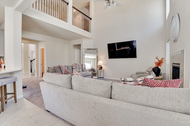 living room with ceiling fan, light colored carpet, a fireplace, and a towering ceiling