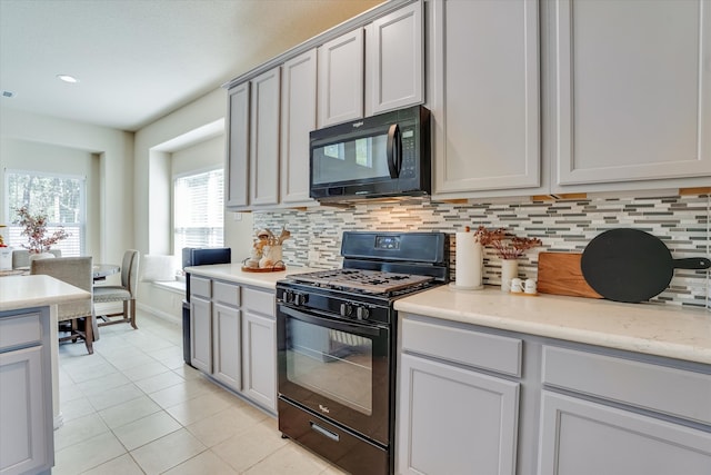 kitchen featuring gray cabinetry, backsplash, light stone countertops, light tile patterned floors, and black appliances