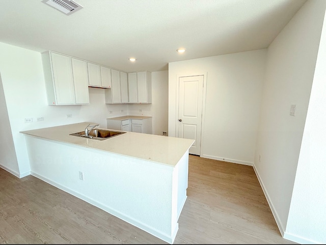 kitchen with white cabinets, kitchen peninsula, sink, and light hardwood / wood-style flooring