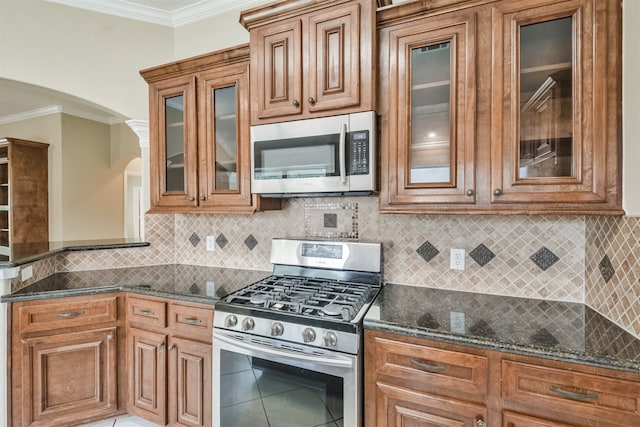 kitchen featuring dark stone countertops, stainless steel appliances, crown molding, and decorative backsplash