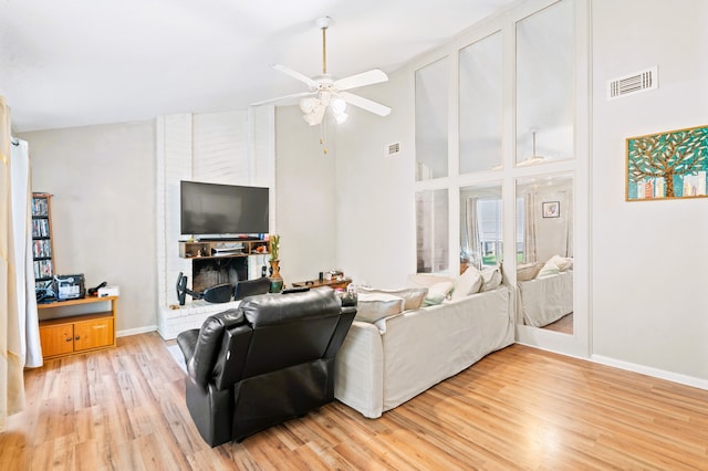 living room featuring high vaulted ceiling, a brick fireplace, light hardwood / wood-style floors, and ceiling fan