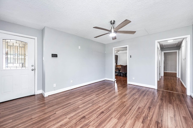 unfurnished bedroom featuring baseboards, a textured ceiling, attic access, a ceiling fan, and wood finished floors