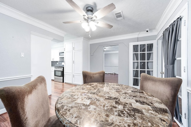 dining space with visible vents, ceiling fan, ornamental molding, and wood finished floors