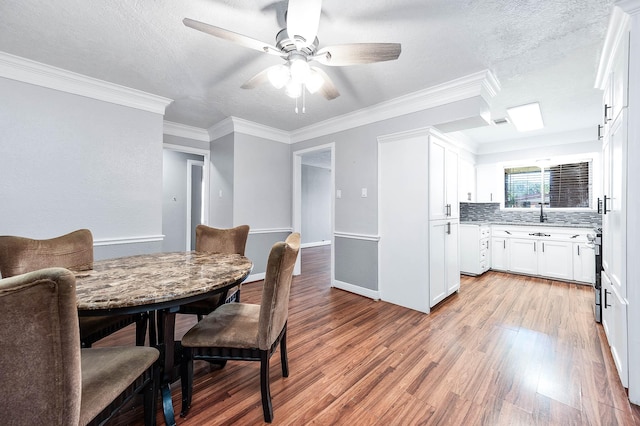 dining room with baseboards, a ceiling fan, light wood-style floors, a textured ceiling, and crown molding