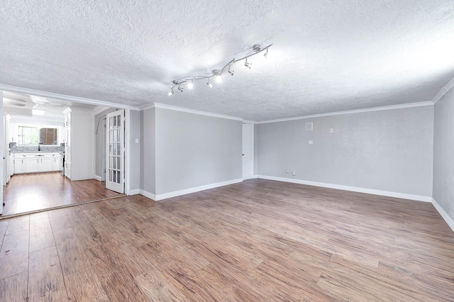 unfurnished living room featuring baseboards, light wood-type flooring, ornamental molding, a textured ceiling, and a sink