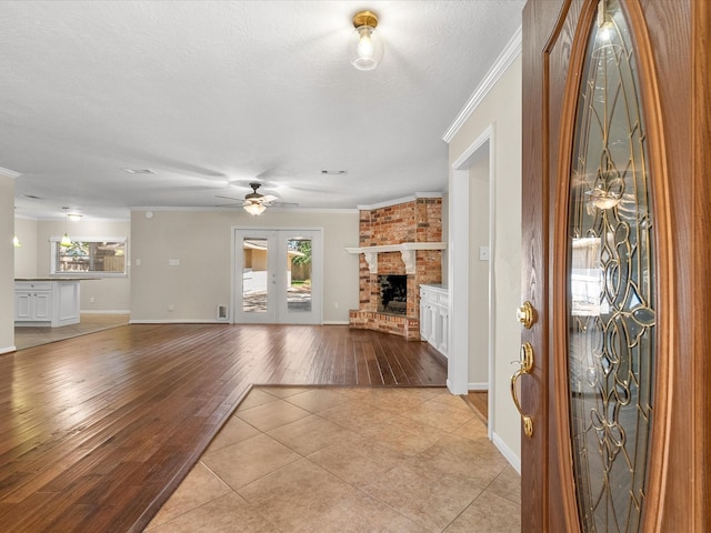 unfurnished living room featuring a textured ceiling, ceiling fan, crown molding, a fireplace, and light tile patterned flooring