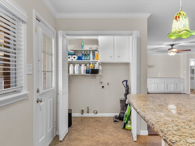 clothes washing area featuring ceiling fan, a healthy amount of sunlight, cabinets, crown molding, and light tile patterned floors