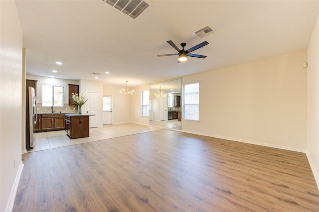 unfurnished living room with sink, ceiling fan with notable chandelier, and light hardwood / wood-style flooring