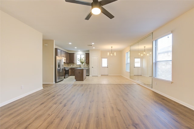 unfurnished living room with sink, ceiling fan with notable chandelier, and light hardwood / wood-style flooring