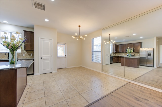 kitchen with stainless steel appliances, a center island, decorative backsplash, a chandelier, and light wood-type flooring