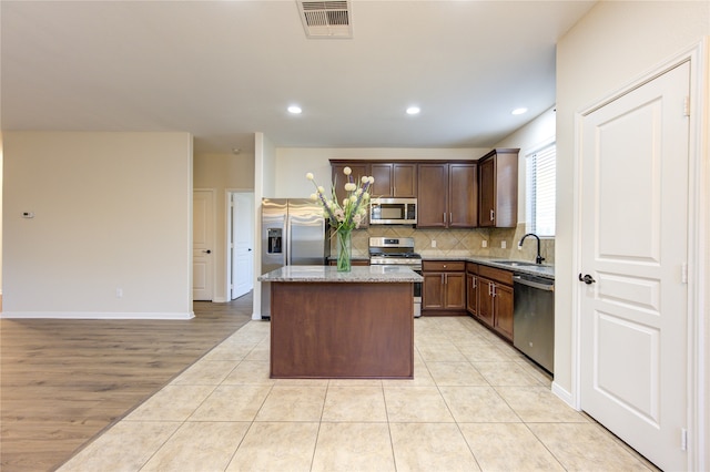 kitchen with light stone counters, a center island, light hardwood / wood-style flooring, sink, and appliances with stainless steel finishes