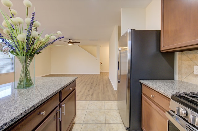 kitchen featuring light stone counters, decorative backsplash, gas range, ceiling fan, and light wood-type flooring