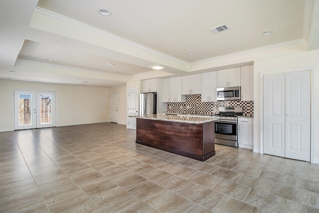 kitchen featuring a raised ceiling, a kitchen island with sink, white cabinetry, appliances with stainless steel finishes, and light stone countertops