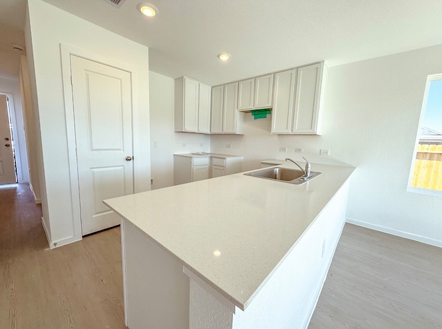 kitchen with kitchen peninsula, sink, white cabinets, and light hardwood / wood-style flooring