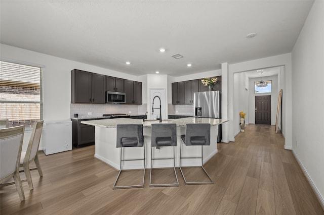 kitchen with decorative backsplash, light hardwood / wood-style floors, an island with sink, stainless steel appliances, and a kitchen bar