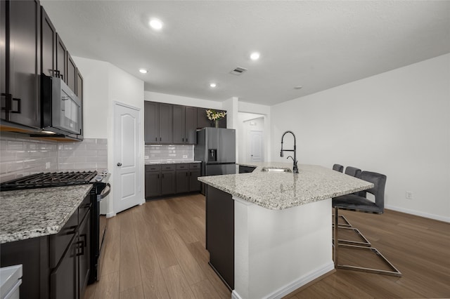 kitchen with light hardwood / wood-style floors, sink, a breakfast bar area, stainless steel appliances, and a center island with sink