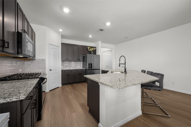 kitchen with wood finished floors, a sink, stainless steel appliances, decorative backsplash, and a breakfast bar area