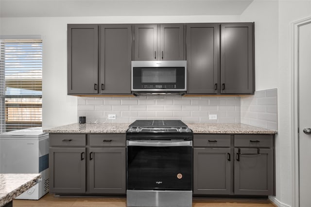 kitchen featuring light stone countertops, stainless steel appliances, and gray cabinetry