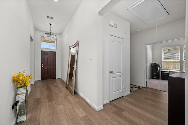 hall with light wood finished floors, visible vents, baseboards, and attic access