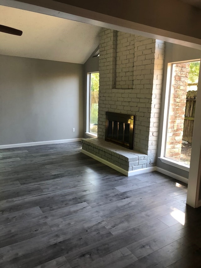 unfurnished living room with lofted ceiling with beams, a brick fireplace, plenty of natural light, and dark wood-type flooring