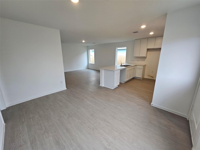 kitchen with white cabinetry, light hardwood / wood-style floors, kitchen peninsula, and sink