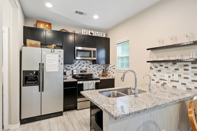 kitchen featuring decorative backsplash, light hardwood / wood-style floors, light stone countertops, stainless steel appliances, and sink