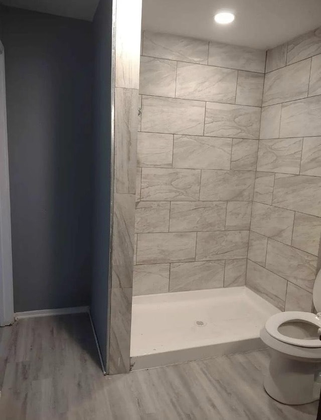 bathroom featuring toilet, hardwood / wood-style floors, and tiled shower