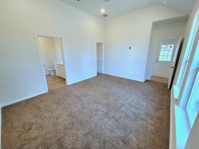 unfurnished bedroom with connected bathroom, vaulted ceiling, and light carpet