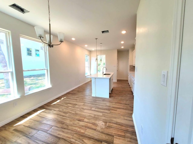 kitchen featuring a center island with sink, white cabinets, decorative light fixtures, and light wood-type flooring