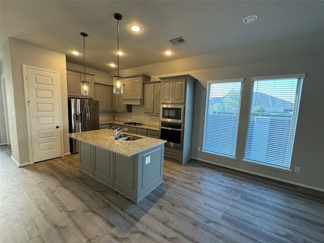 kitchen featuring wood-type flooring, pendant lighting, a center island with sink, and stainless steel appliances