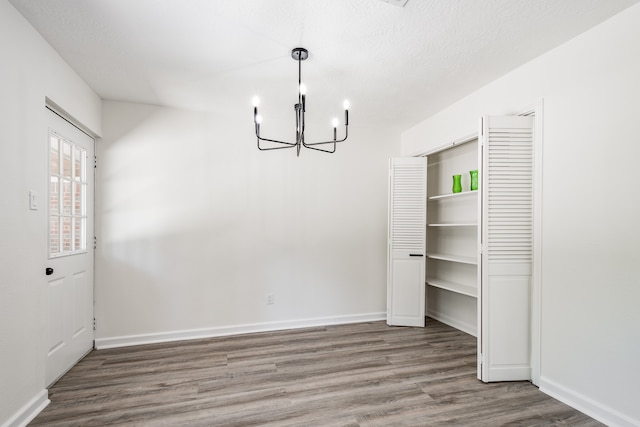 unfurnished dining area with a textured ceiling, wood-type flooring, and an inviting chandelier