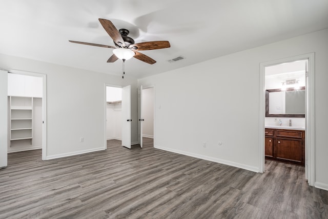 unfurnished bedroom with ceiling fan, a walk in closet, a closet, light wood-type flooring, and ensuite bathroom