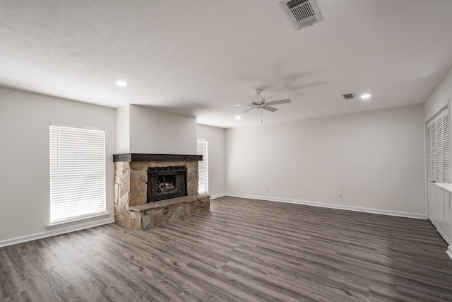 unfurnished living room featuring a textured ceiling, ceiling fan, dark hardwood / wood-style floors, and a stone fireplace