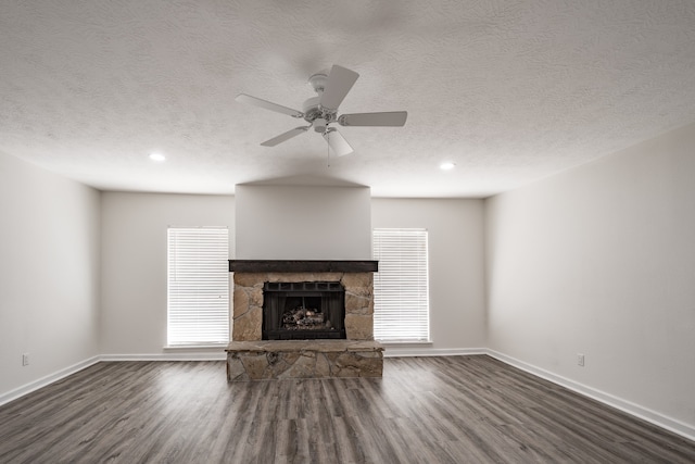 unfurnished living room with ceiling fan, a stone fireplace, dark hardwood / wood-style floors, and a healthy amount of sunlight