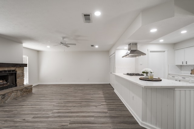 kitchen with ceiling fan, white cabinets, wall chimney exhaust hood, dark wood-type flooring, and a fireplace