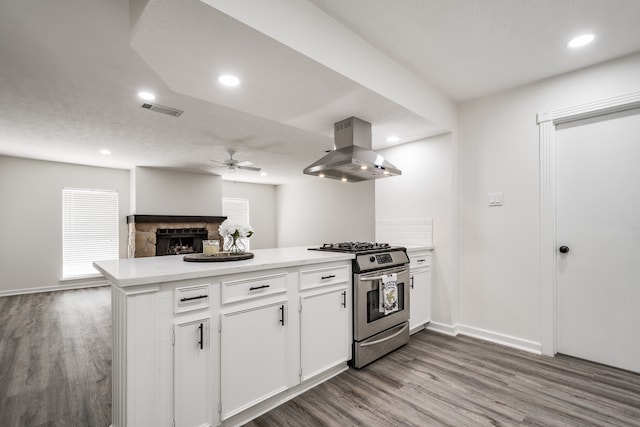 kitchen featuring white cabinets, a stone fireplace, stainless steel range with gas cooktop, ceiling fan, and extractor fan