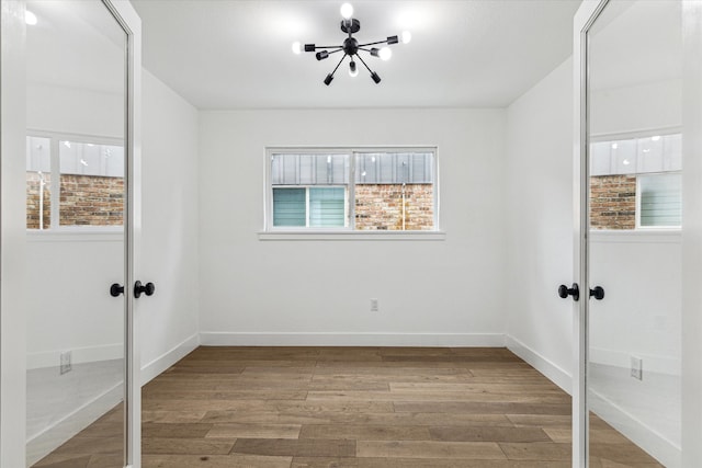 empty room featuring french doors, a notable chandelier, and hardwood / wood-style floors