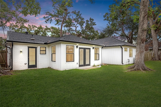 back house at dusk with a lawn and french doors