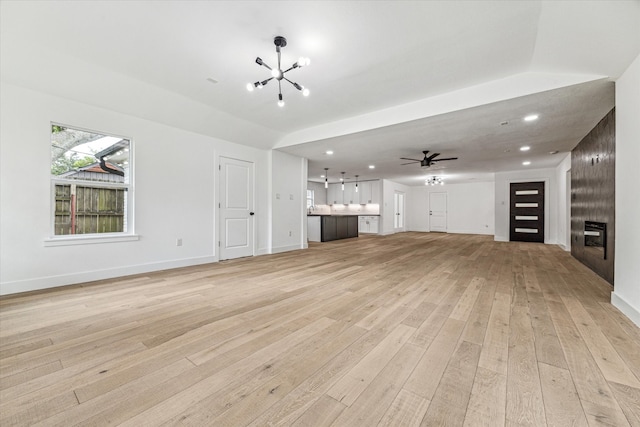 unfurnished living room featuring ceiling fan with notable chandelier, a fireplace, and light hardwood / wood-style floors