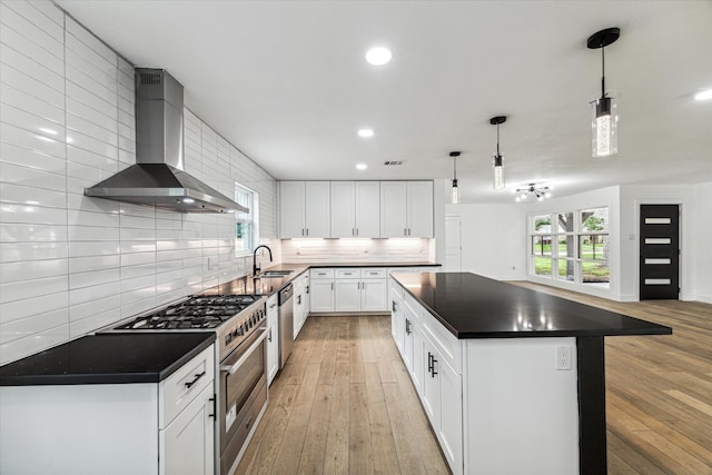 kitchen with white cabinets, hanging light fixtures, wall chimney range hood, a center island, and light wood-type flooring