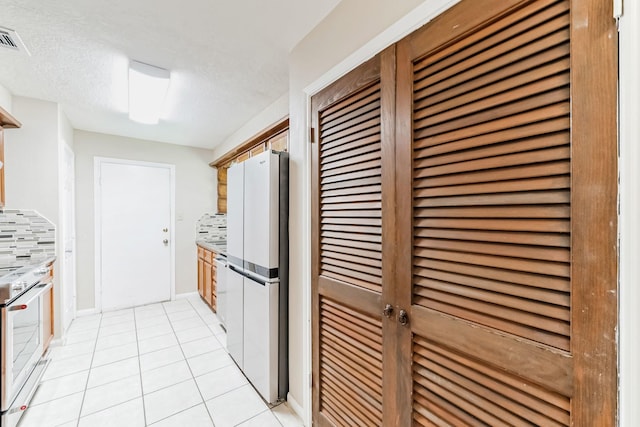 kitchen with light tile patterned flooring, a textured ceiling, white appliances, and backsplash