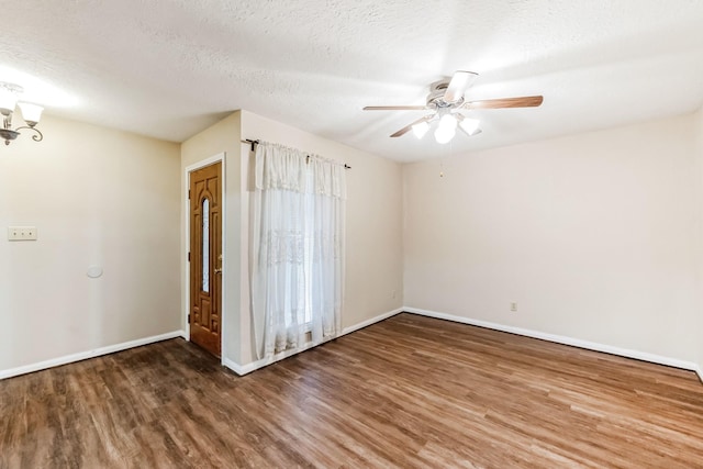 spare room with a textured ceiling, ceiling fan with notable chandelier, and dark wood-type flooring