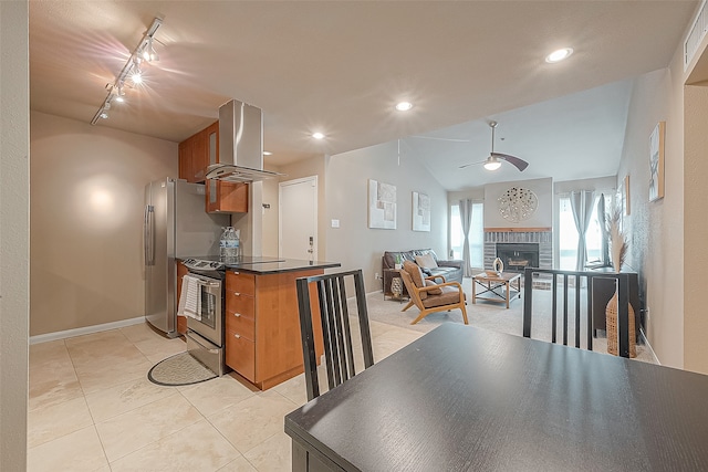 kitchen with island range hood, rail lighting, a brick fireplace, appliances with stainless steel finishes, and ceiling fan