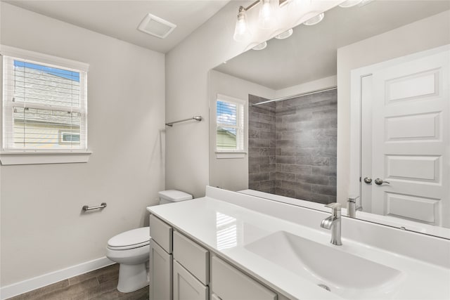 bathroom featuring hardwood / wood-style floors, vanity, toilet, and a tile shower