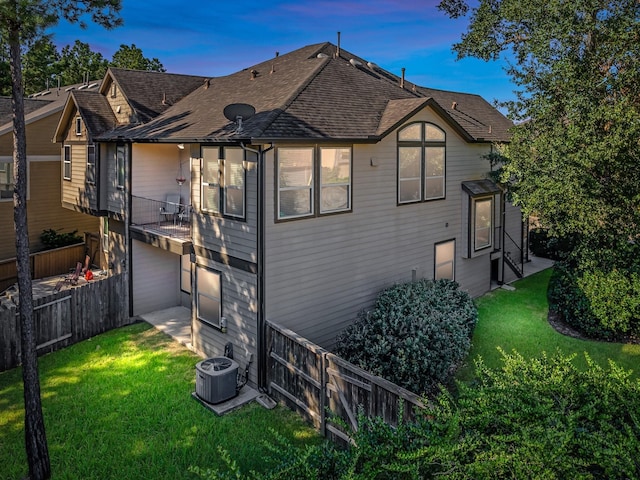 back house at dusk with central air condition unit, a garage, and a yard