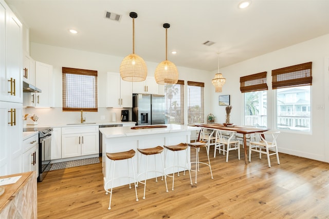 kitchen featuring appliances with stainless steel finishes, hanging light fixtures, light hardwood / wood-style flooring, a center island, and white cabinets