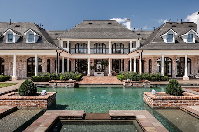 back of house with a balcony, a swimming pool with hot tub, and a patio