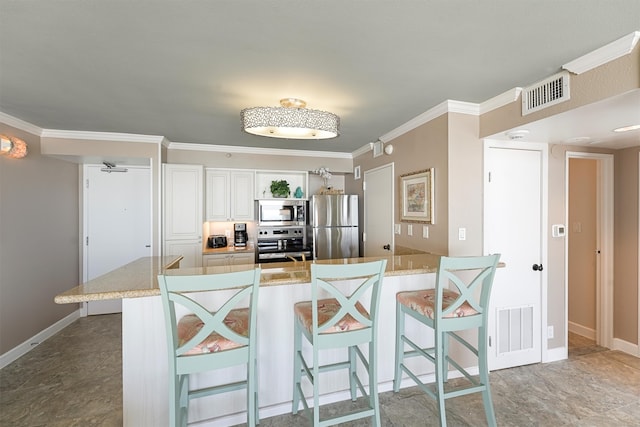 kitchen with white cabinets, a kitchen bar, ornamental molding, and stainless steel appliances