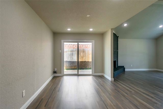 spare room featuring a brick fireplace and dark hardwood / wood-style flooring